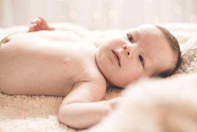 A diapered baby lays on a beige blanket