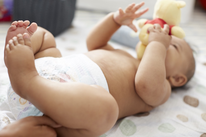 A diapered baby lays on a spotted blanket holding a toy close to its face