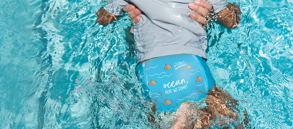 Un padre sostiene a su bebé que tiene puesto un calzoncito de natación Huggies Little Swimmers con el diseño de Buscando a Nemo mientras chapotean en una piscina