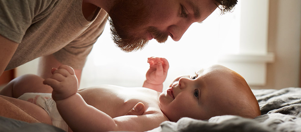 Un padre se prepara para tomar a su bebé sonriente que está sobre una manta