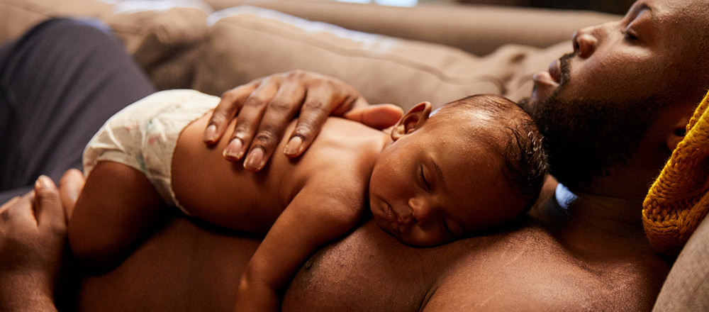 A diapered baby laying on their sleeping father's chest