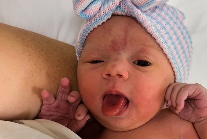 Newborn baby, Lana, sticking her tongue out with a knit beanie on her head