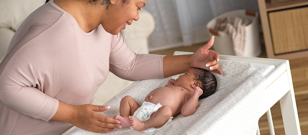 A mother smiles down on her diapered baby on a changing table