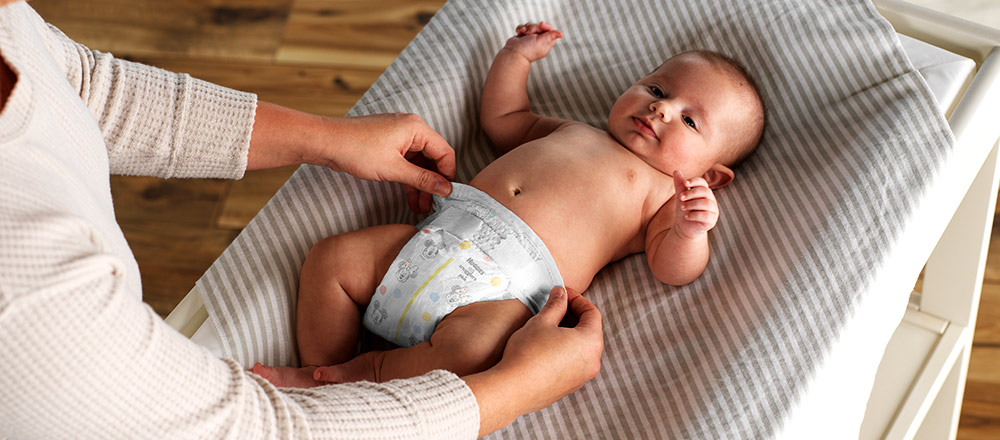A parent puts a Huggies Little Snugglers Plus Diaper on their baby laying on a changing table