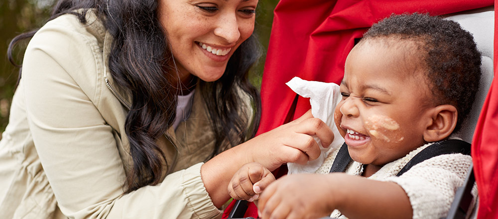 A smiling mother reaches to wipe a laughing baby's messy face with a Huggies Natural Care Refreshing Wipe