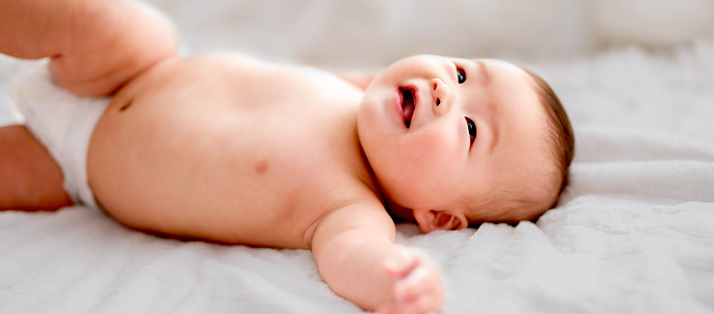 A diapered baby laying on a white blanket