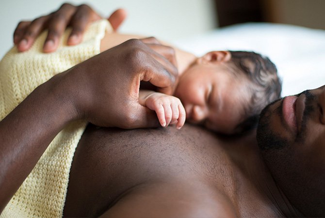Baby sleeping on dad’s chest in comfy bed.